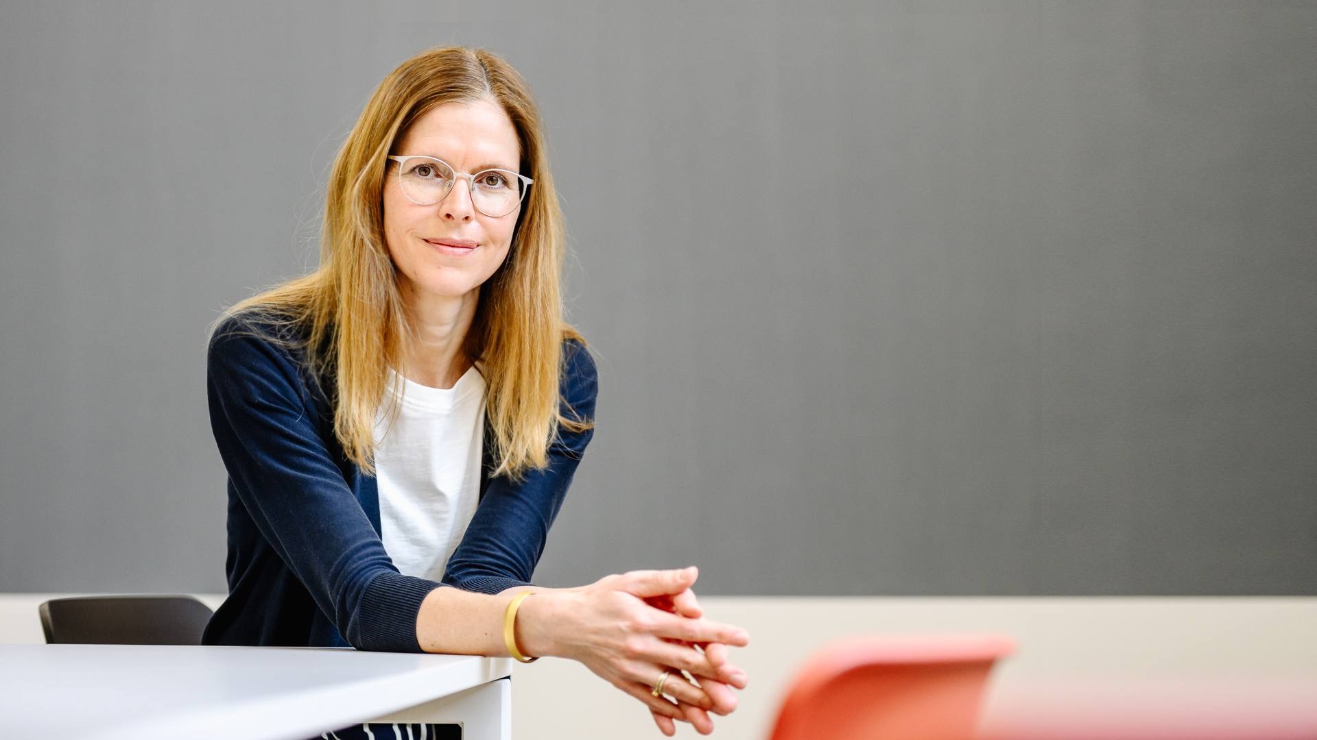 Dr. Isabell Osann, Coach im Coaching Kontext, An einem Tisch sitzend, ruhig blickend, mit einer Tafel im Hintergrund.