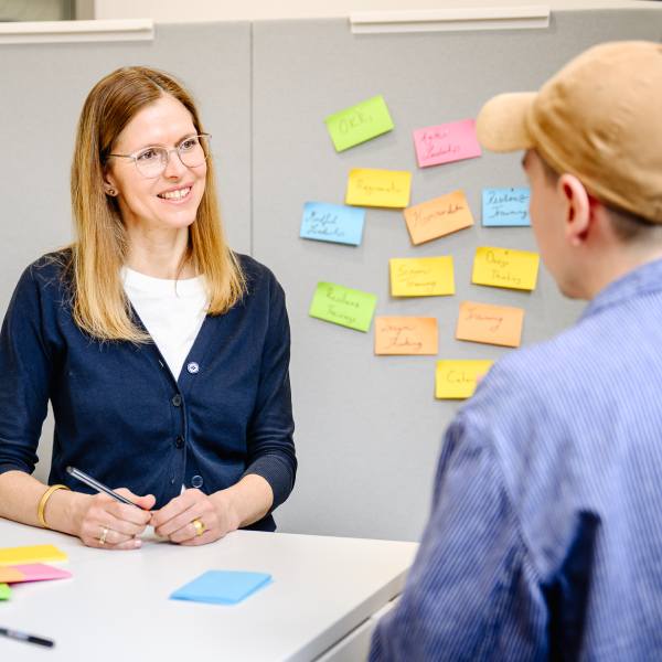 Dr. Isabell Osann, Coach im Coaching Kontext, an einem Tisch stehend, im Gespräch mit einem Seminar Teilnehmer.