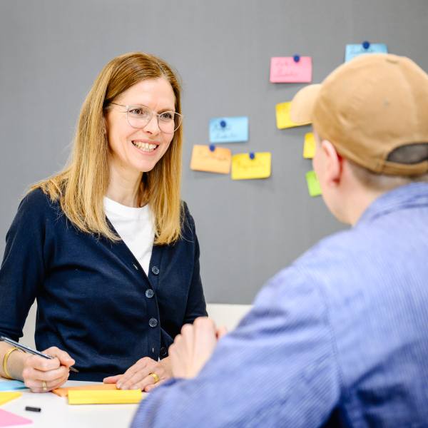 Dr. Isabell Osann, Coach im Coaching Kontext, an einem Tisch stehend, im Gespräch mit einem Seminar Teilnehmer.